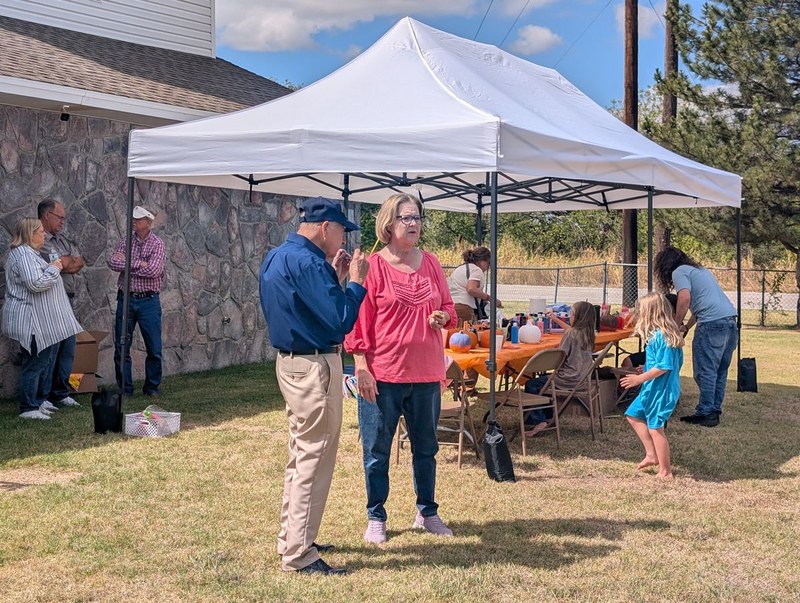 Adults and children sharing an outdoor gathering beside Wheatland’s stone church building.