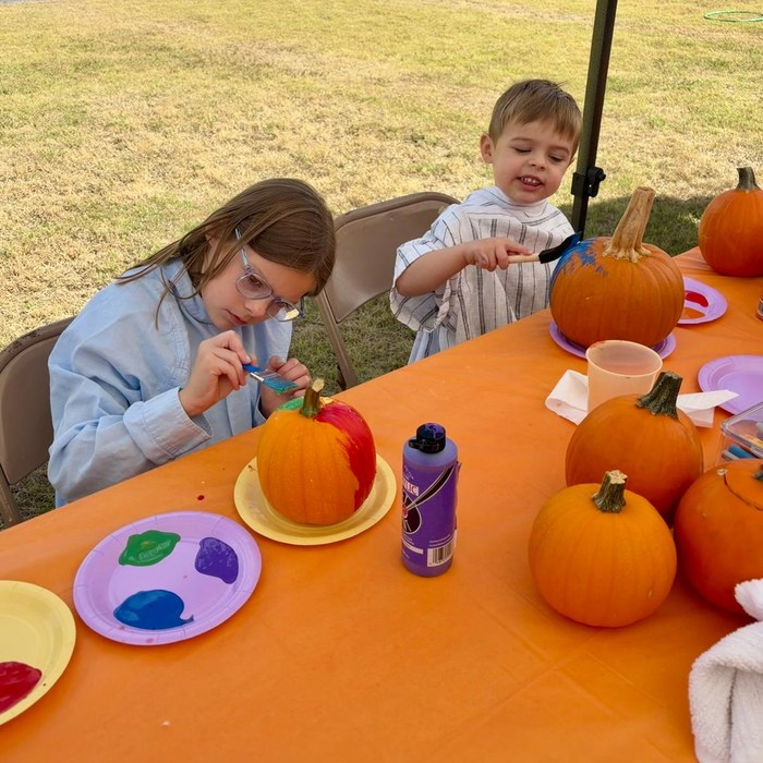 Two children carefully painting pumpkins at an orange-covered table during Wheatland’s fall fellowship.